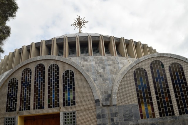A domed Ethiopian Orthodox cathedral with stained-glass arches and a metal cross on the roof