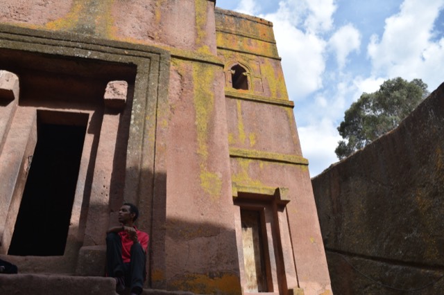 A rock-hewn church at Lalibela carved down into red stone, lichen spreading across its walls