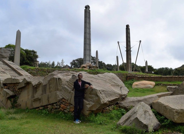 Toppled granite stelae lying in the grass at Axum, with carved obelisks still standing behind