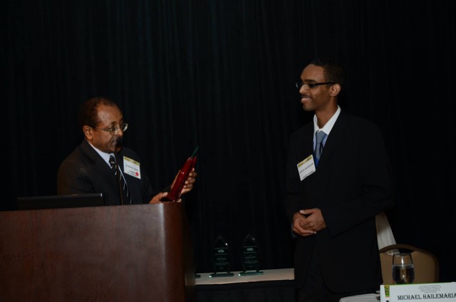 An award being presented at a ceremony podium in front of a dark curtain